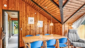 Un interior de madera con una gran mesa de comedor, sillas azules, un sofá gris y un techo de madera.