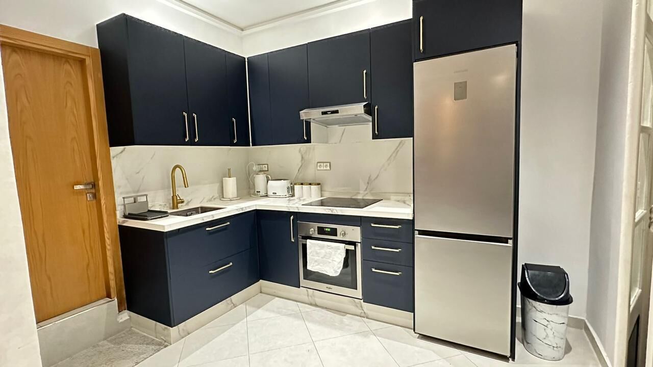 A modern kitchen with dark cabinets, stainless steel appliances, and a marble countertop.
