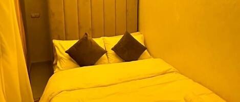 Una habitación de hotel con cama, almohadas y una lámpara en el techo.