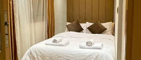 A hotel room with a bed, a ceiling light, and a curtain.