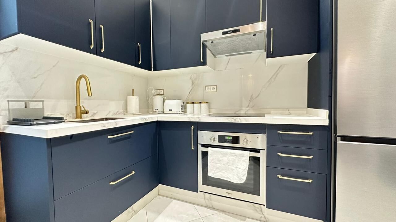 A modern kitchen with dark blue cabinets, a stainless steel refrigerator, a built-in oven, and a white marble countertop.