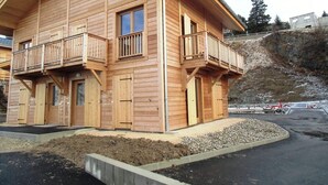A two-story wooden cabin with balconies, a concrete foundation, and a gravel driveway. - Attached chalet for 8 on 3 levels, pets allowed (Chamrousse)