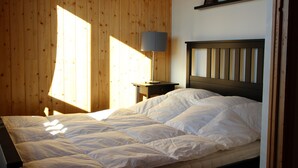 A bedroom with a wooden wall, a bed with white bedding, a nightstand with a lamp, and a framed picture on the wall. - Attached chalet for 8 on 3 levels, pets allowed (Chamrousse)
