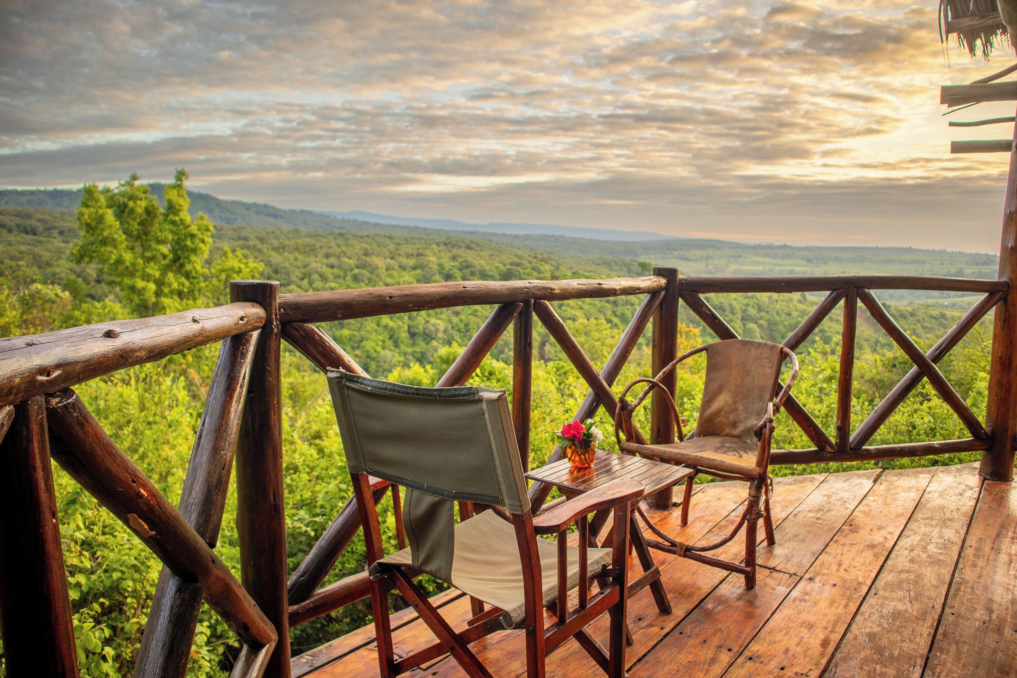 A wooden deck with two chairs and a small table, overlooking a lush green landscape.