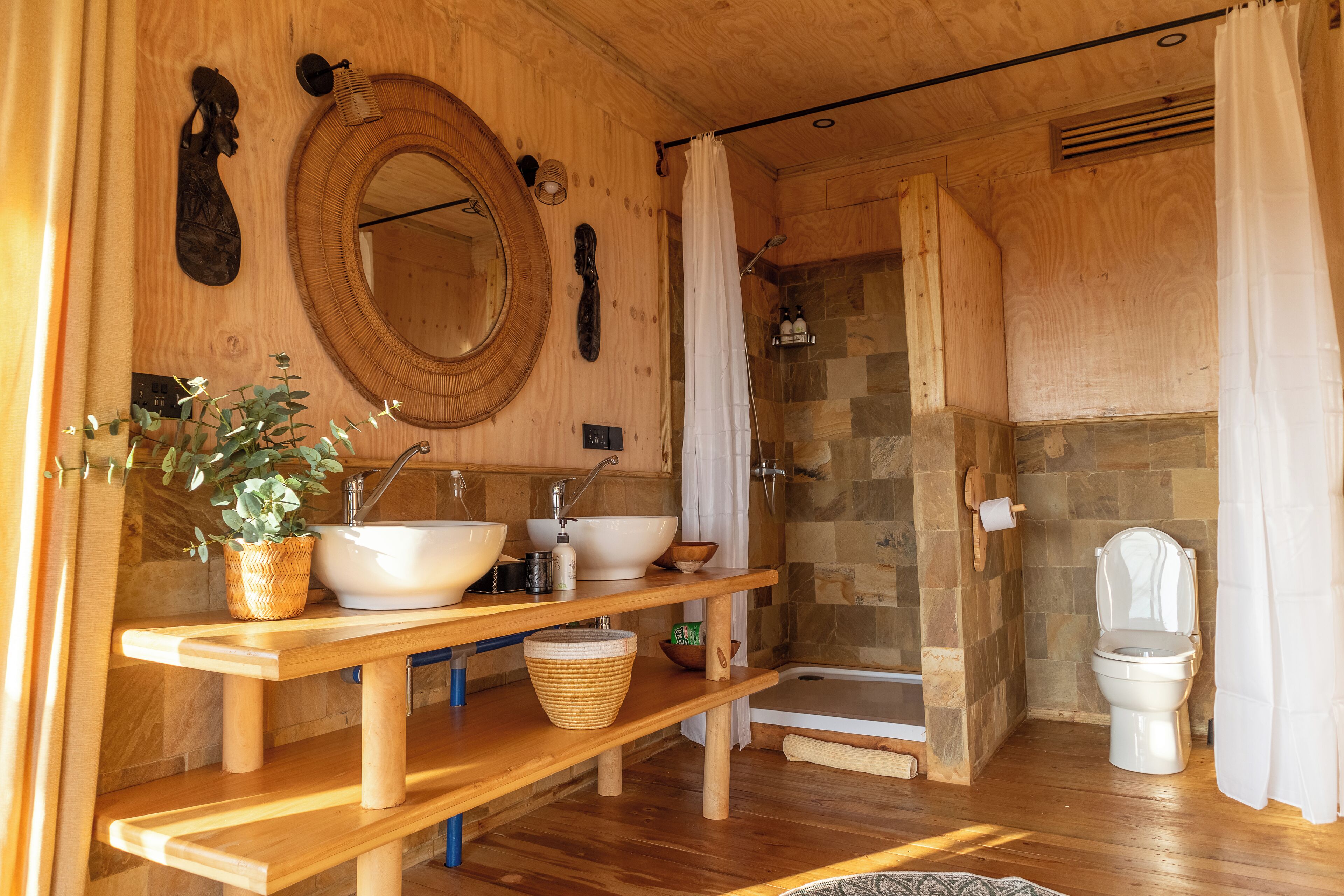 Een houten badkamer met een grote spiegel, twee wastafels, een douche en een toilet.