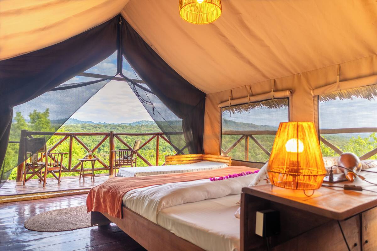 A tented accommodation with a bed, a table, chairs, and a view of the landscape.