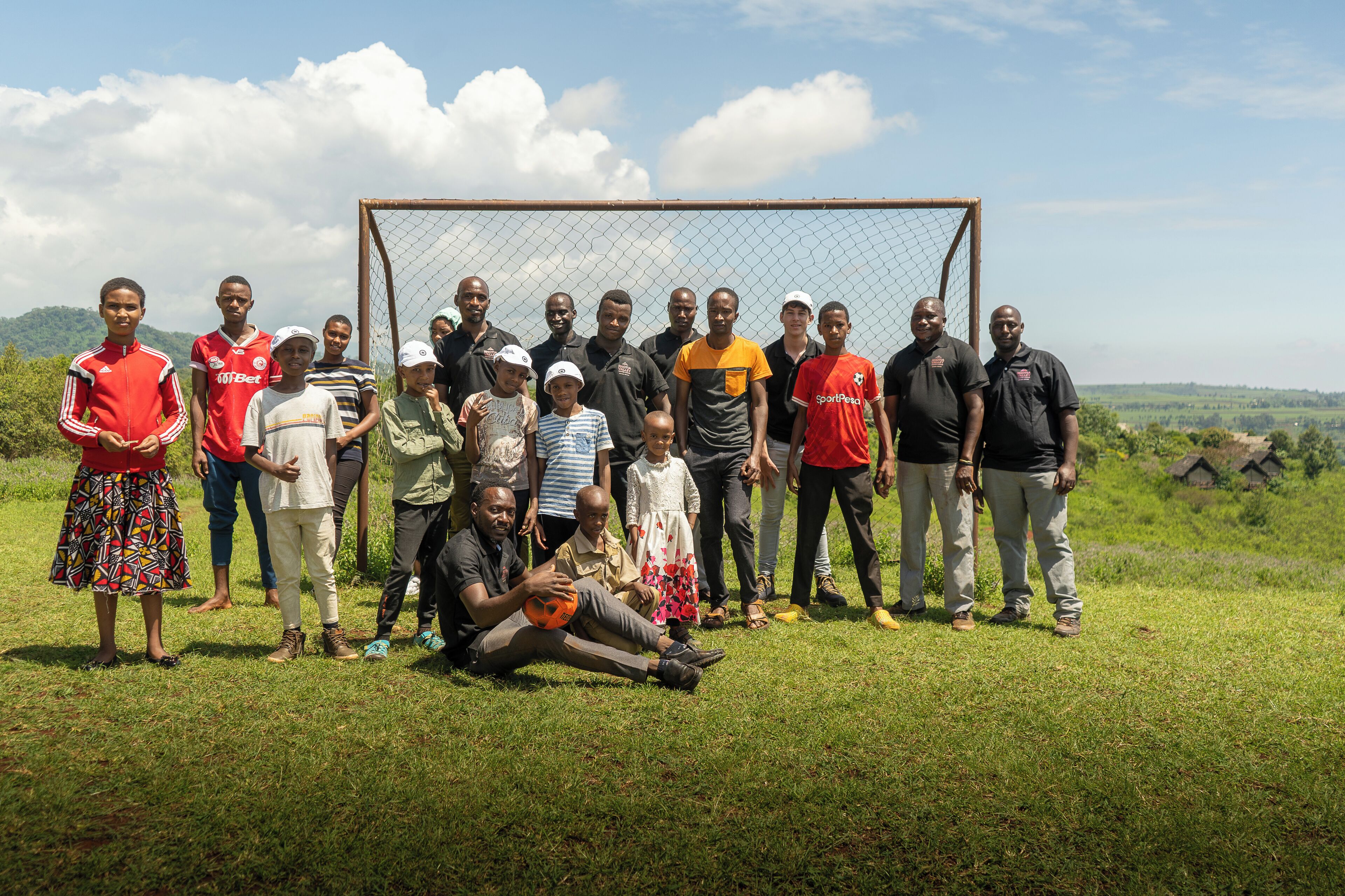 Un groupe de personnes se tient dans un champ d’herbe, avec un but de football en arrière-plan.