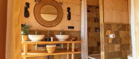 A wooden bathroom with a round mirror, two sinks, a shower, and a toilet.