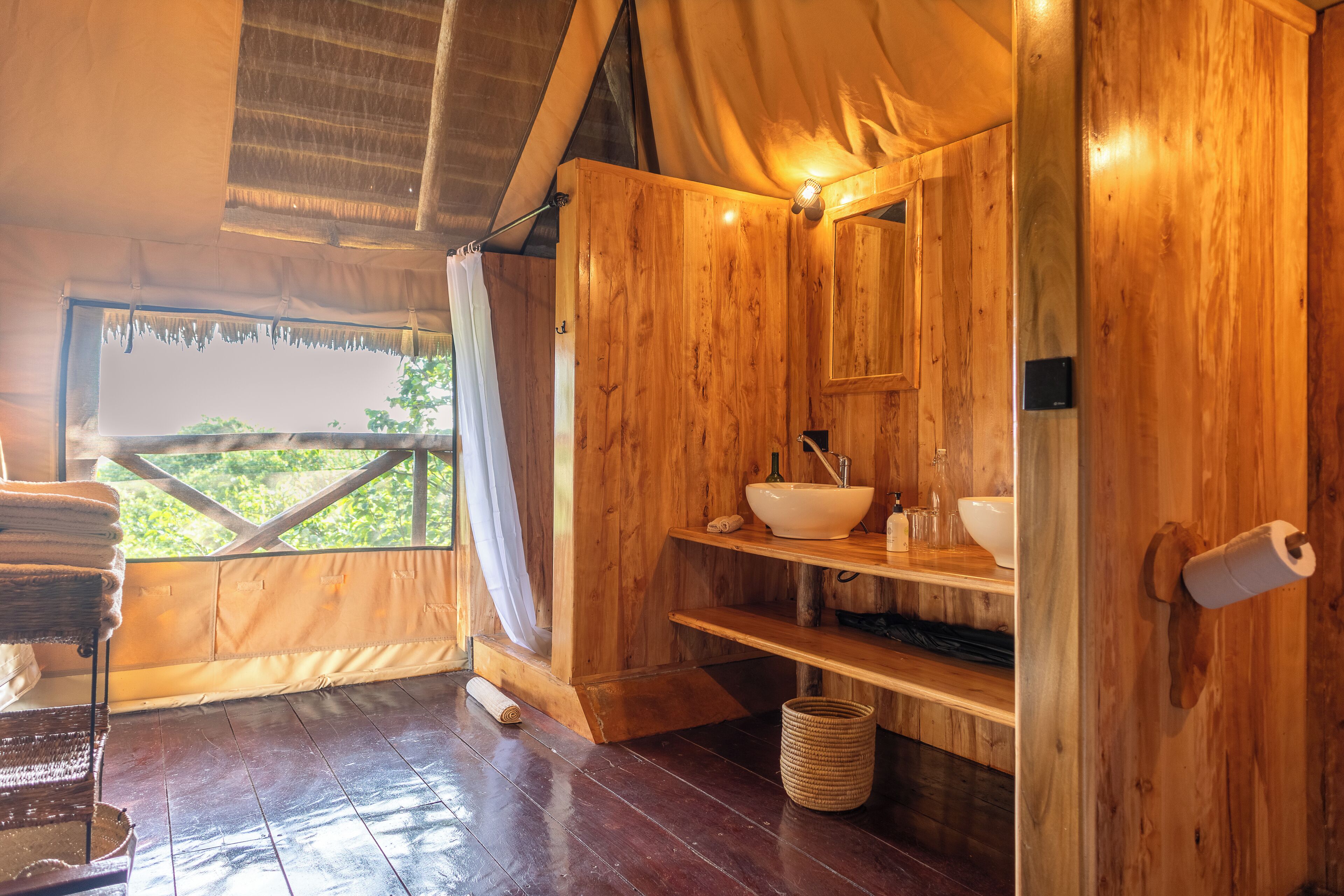 Een houten hut met een houten wastafel, planken en een raam met uitzicht op groen.