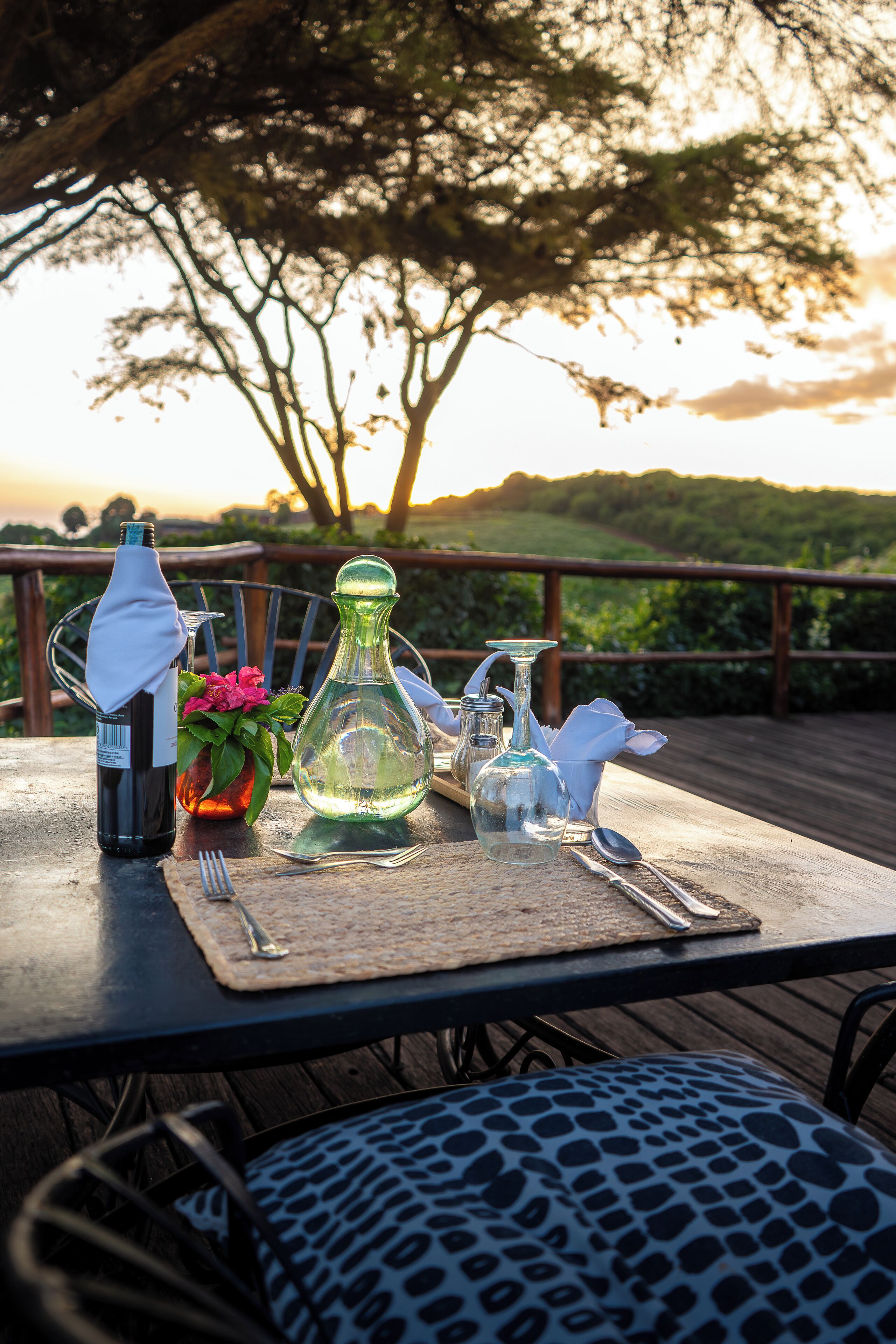 A table set outdoors with a bottle, glassware, and a flower vase.