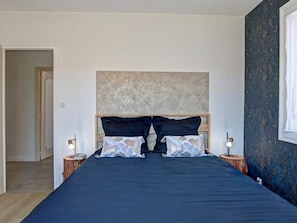 A bedroom with a large bed, two bedside tables with lamps, a headboard, and a door leading to another room.