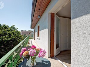 A balcony with a green railing, a table with a vase of flowers, and a building with a white exterior and a wooden roof.