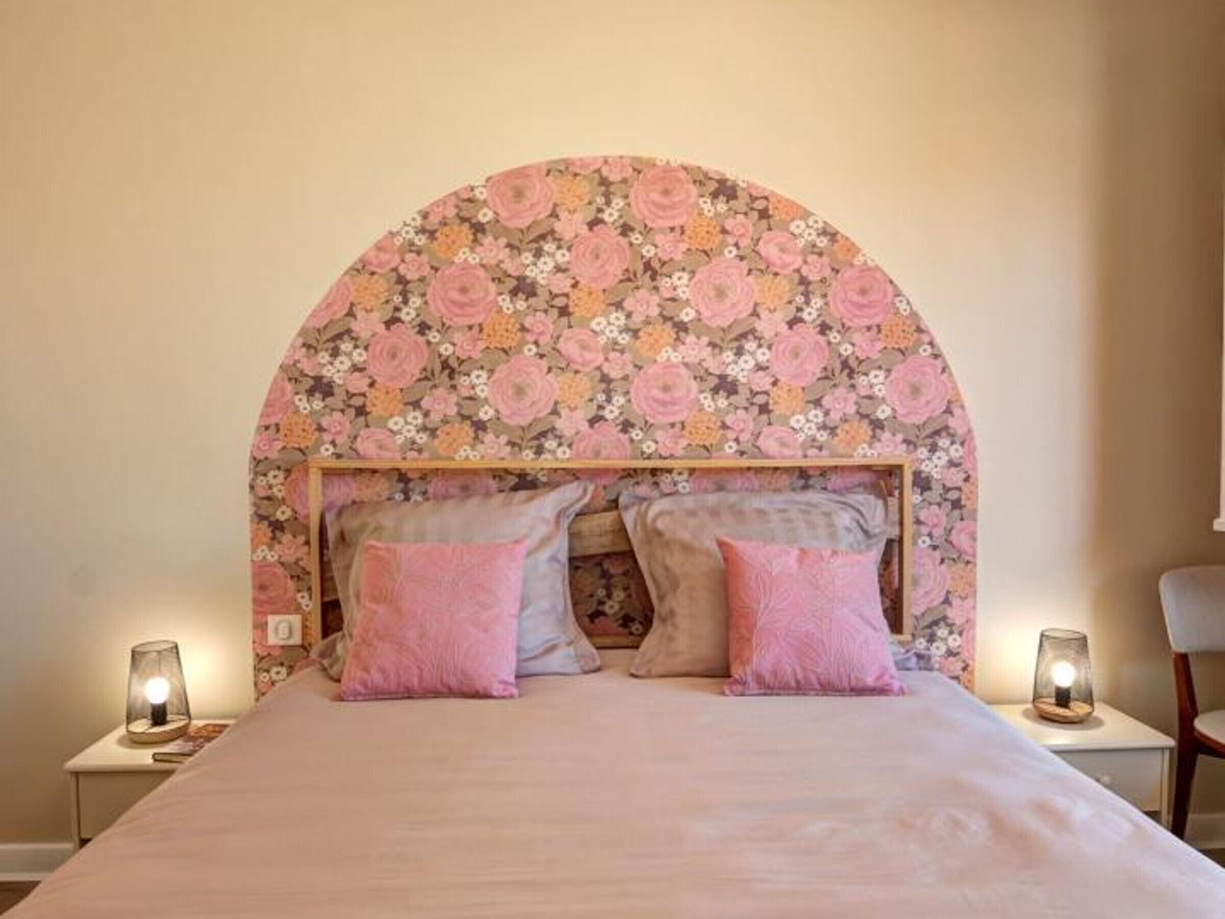 A bedroom with a floral headboard, two bedside lamps, and a bed with pink pillows.