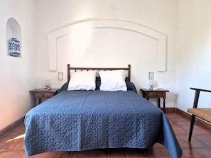 A bedroom with a bed, two bedside tables, a chair, and a wall-mounted shelf.