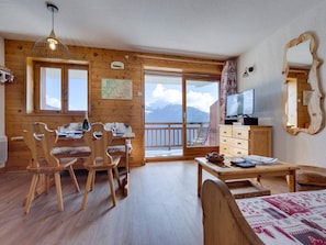 A wooden interior with a dining area, a TV, and a view of mountains.