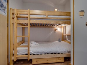 Uma cama beliche com escada, uma prateleira pequena e um ponto de luz fixado na parede.