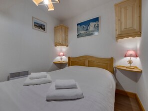A bedroom with a wooden headboard, two bedside tables with lamps, a bed with white linens, and two framed pictures on the wall.