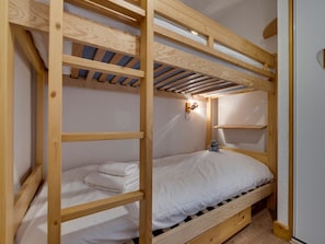Un lit superposé avec une structure en bois, une literie blanche et une petite table de chevet avec une lampe.