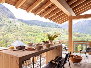 Terraza de madera con una mesa lista para el desayuno, con vistas a un paisaje montañoso.