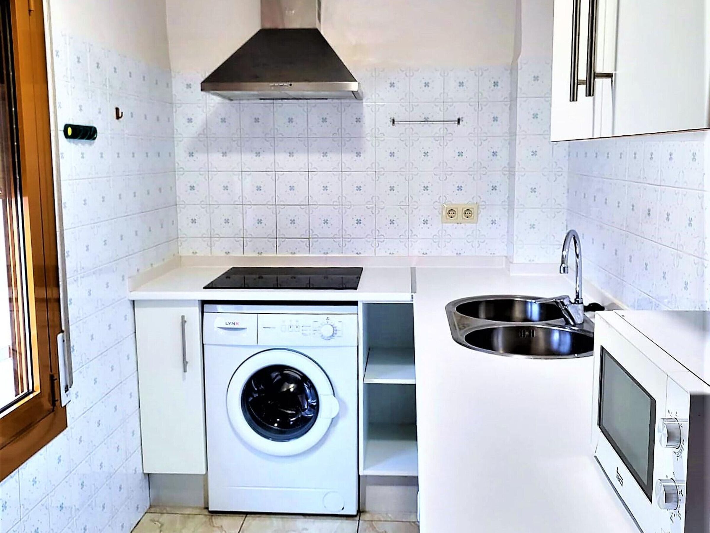 A compact kitchen with a washing machine, a stove, and a sink.