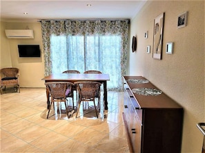 Uma área de refeições com mesa e cadeiras, balcão de cozinha e TV fixada na parede.
