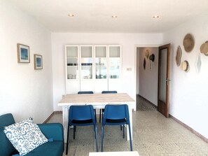 Un coin repas avec une table et des chaises, un canapé agrémenté d’un coussin à motifs, et un couloir avec une porte et des éléments de décoration murale.