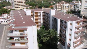 A multi-story residential building with balconies, a parking area, and a palm tree.