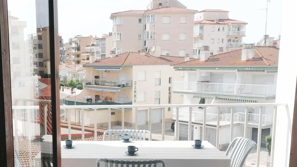 A balcony with a table and chairs, overlooking a residential area with multiple buildings.