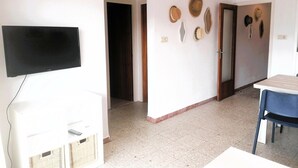 A room with a flat-screen TV, a table, and chairs, and a wall with hats.