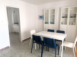 Uma sala de jantar com uma mesa branca, cadeiras azuis e armários brancos com portas de vidro.