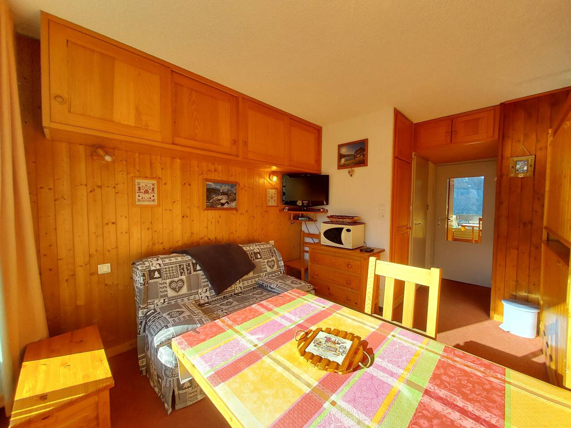 Una habitación acogedora con paredes de madera, una cama con ropa de cama estampada, una mesa con mantel colorido, un televisor y un microondas.