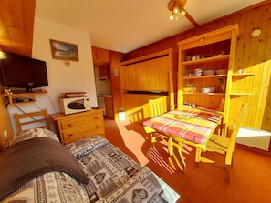 A cozy room with a bed, a television, a microwave, a dining table with chairs, and wooden cabinets. - Cozy 17m² studio for 2 in Plan Peisey, pets allowed (Peisey-Nancroix-Plan Peisey)