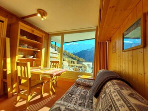 En mysig stuga byggd av trä, med ett matområde, en soffa och ett stort fönster med utsikt över bergen.