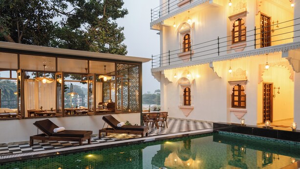 A hotel with a pool area, including lounge chairs and a dining area with tables and chairs. - The Experience Resort (Udaipur)