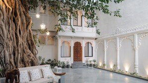 A spacious courtyard with a large tree trunk, a wooden bench, and a traditional building with ornate doors and columns. - The Experience Resort (Udaipur)