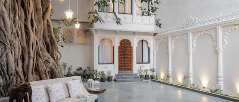 A spacious courtyard with a large tree trunk, a wooden bench, and a traditional building with ornate doors and columns.