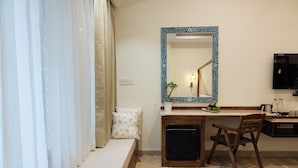 A compact hotel room with a bed, a small desk, a chair, a mirror, and a television. - The Experience Resort (Udaipur)