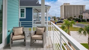 A balcony with two wicker chairs and a view of a building and road.