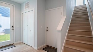 A modern interior with a wooden staircase, white doors, and a view of the outdoors.