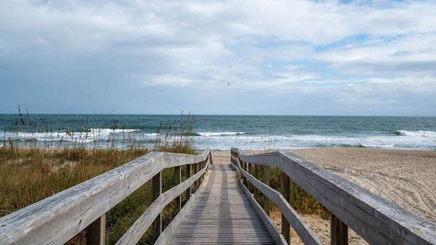 A wooden boardwalk leading to a beach with waves and a clear sky.
