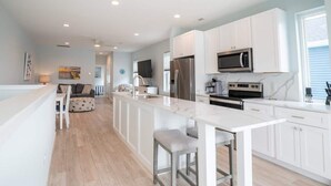 A modern kitchen with white cabinetry, stainless steel appliances, and a central island with stools.