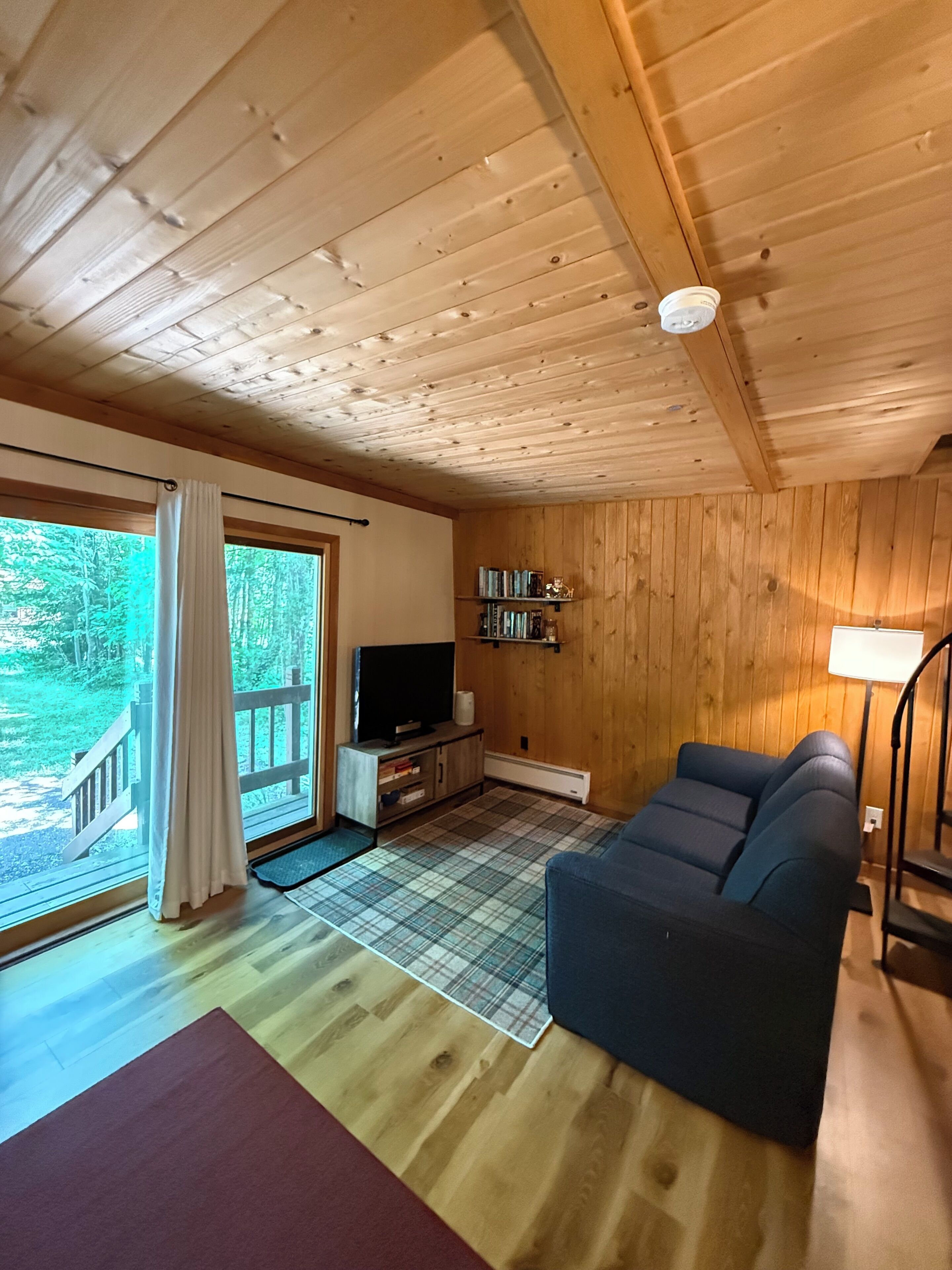 Un interior de madera con un sofá, televisor y una estantería.