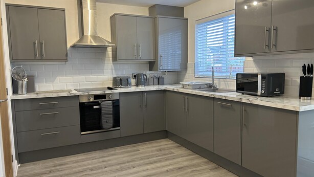 A modern kitchen with grey cabinets, a built-in oven, a microwave, and a window with blinds. - Tranquil Sheffield Retreat - 3 Bedroom House (Sheffield)