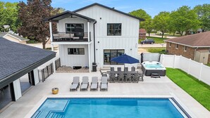 Una casa de dos pisos con piscina en el patio trasero, jacuzzi y terraza con mobiliario exterior.