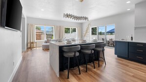 A modern kitchen with a central island, bar stools, and a dining area.