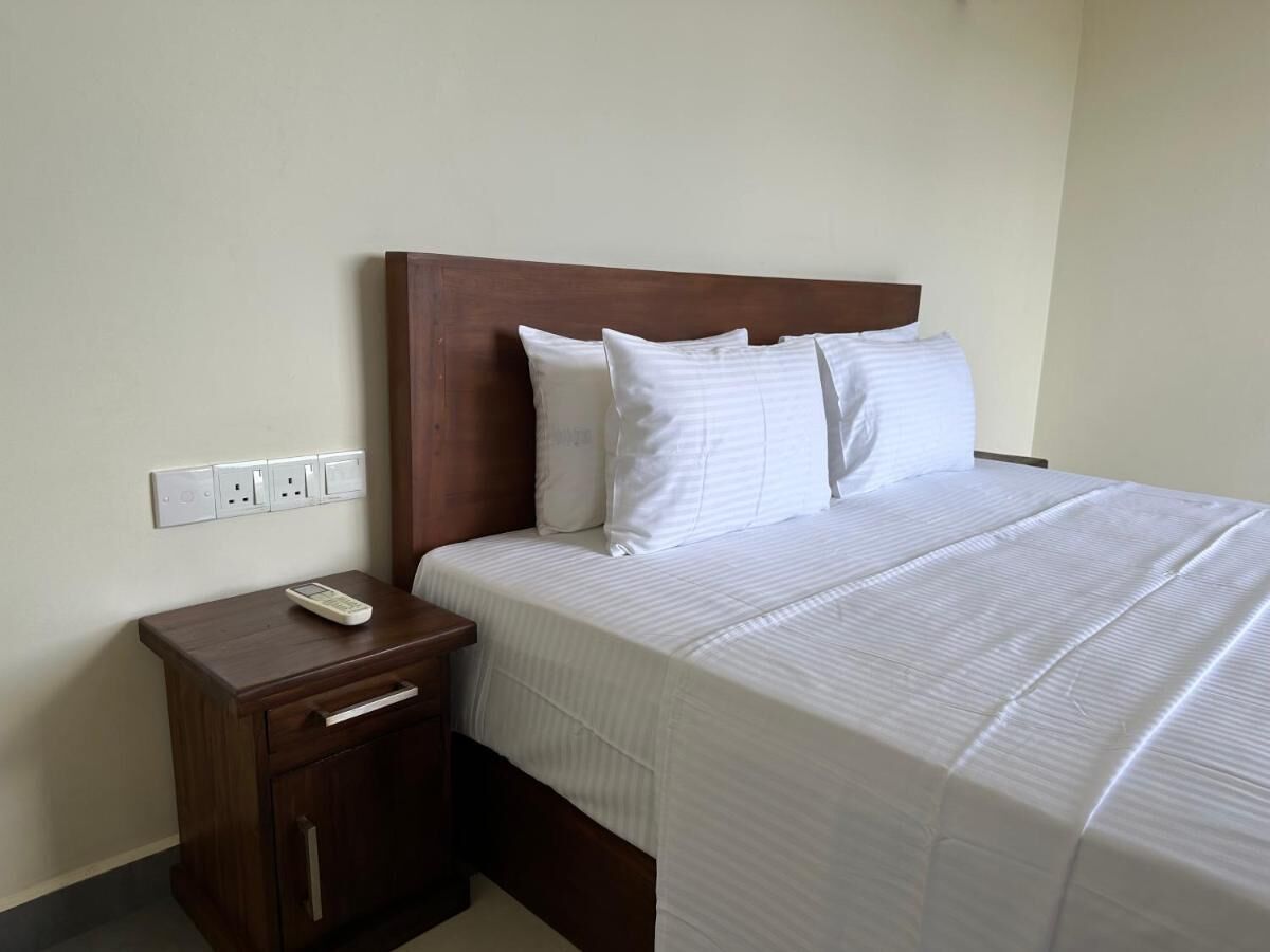 A hotel room with a wooden headboard, a single bed with white bedding, a nightstand with a remote control, and a drawer.
