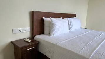 A hotel room with a wooden headboard, a single bed with white bedding, a nightstand with a remote control, and a drawer.