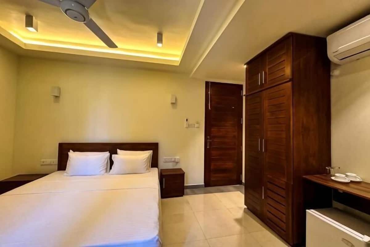 Una habitación de hotel con cama, armario de madera, mesita de noche y aire acondicionado.