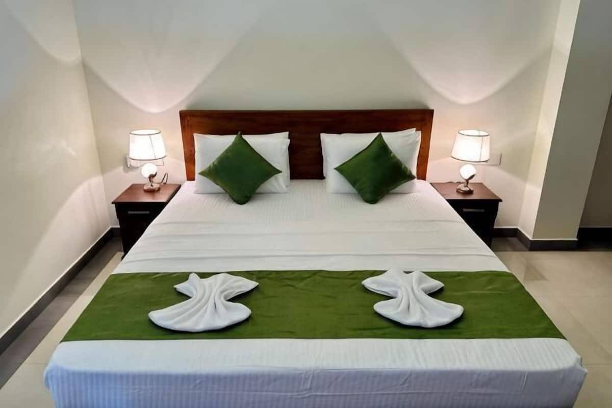 Una cama bien tendida con sábanas blancas, almohadas verdes y dos lámparas de noche.