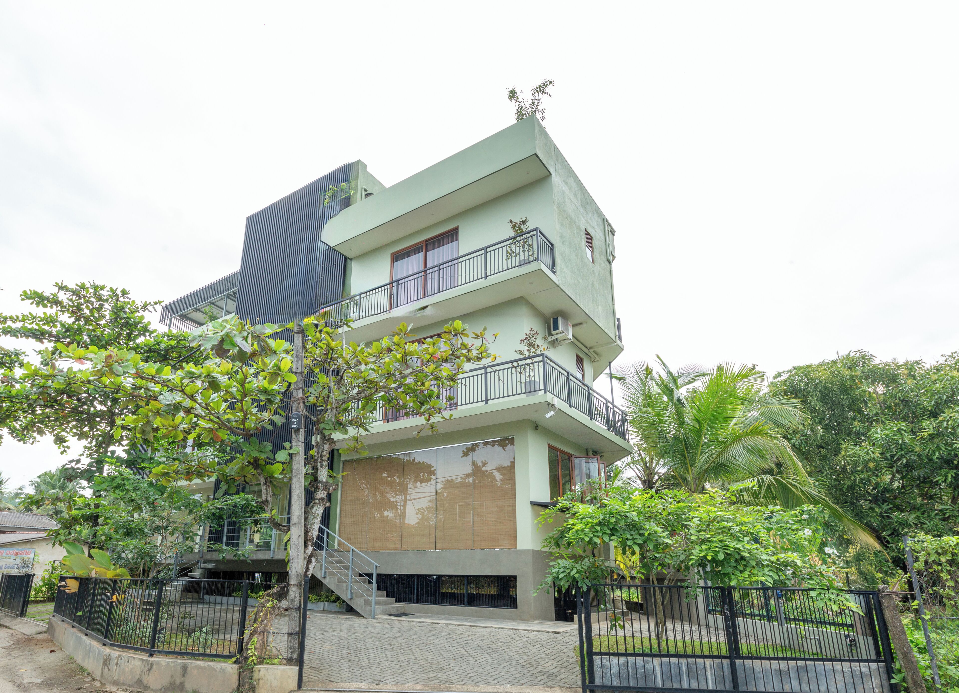 A multi-story building with balconies, a staircase, and surrounding greenery.